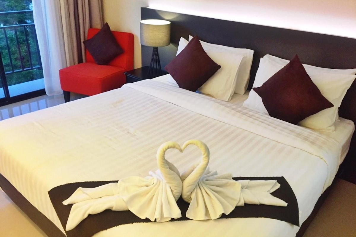 A hotel room with a large bed, a red chair, and a view of the outdoors.