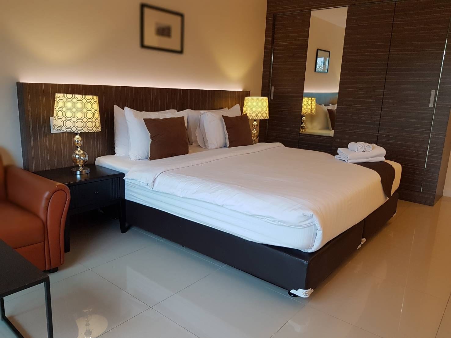 A hotel room with a large bed, two bedside lamps, a nightstand, a chair, and a mirror.