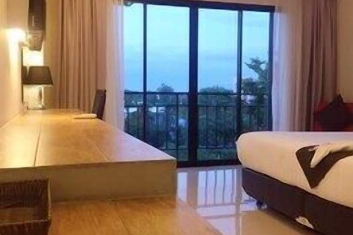 A hotel room with a large bed, a desk, and a view of the city through large windows.