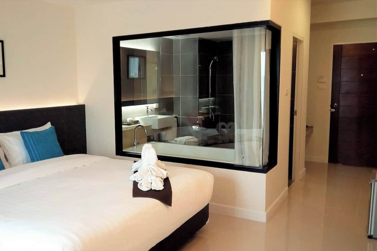 A hotel room with a large bed, a bedside table with a tissue, a framed picture on the wall, and a large mirror reflecting the bathroom.