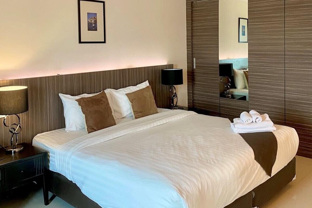 A modern hotel room with a large bed, a nightstand with a lamp, a mirror, and neatly folded towels.