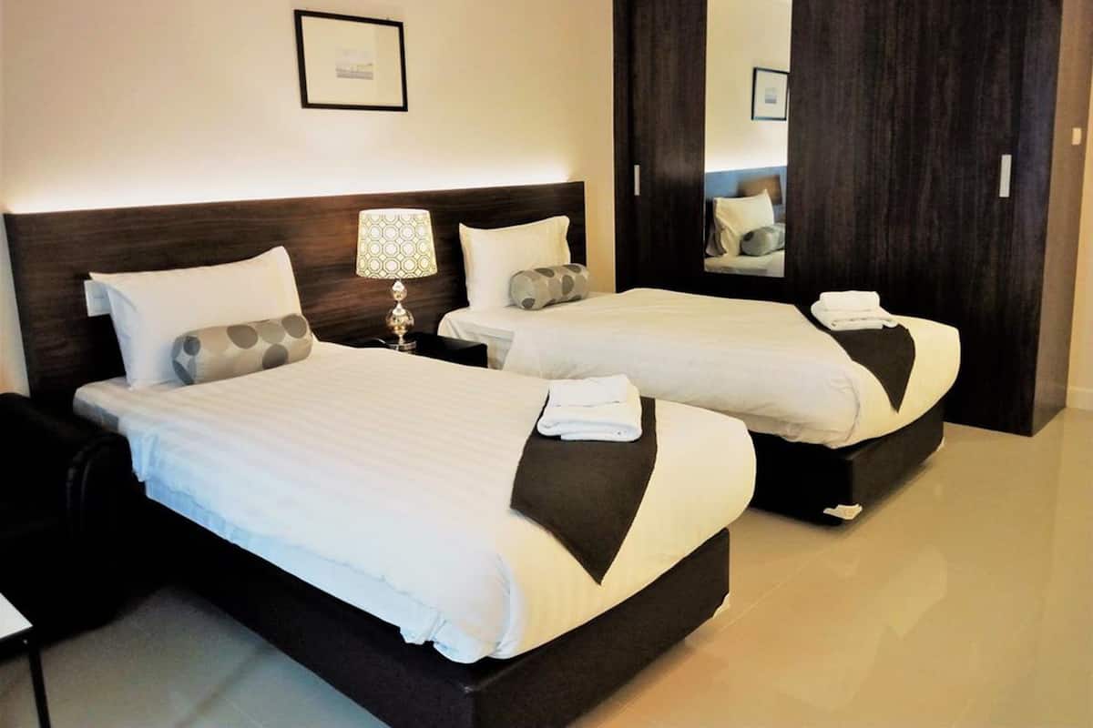 A hotel room with two beds, a nightstand with a lamp, a framed picture on the wall, and a dark wooden wardrobe.