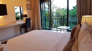 Habitación de hotel con cama, escritorio, silla, televisor y balcón con vistas a árboles y edificios.