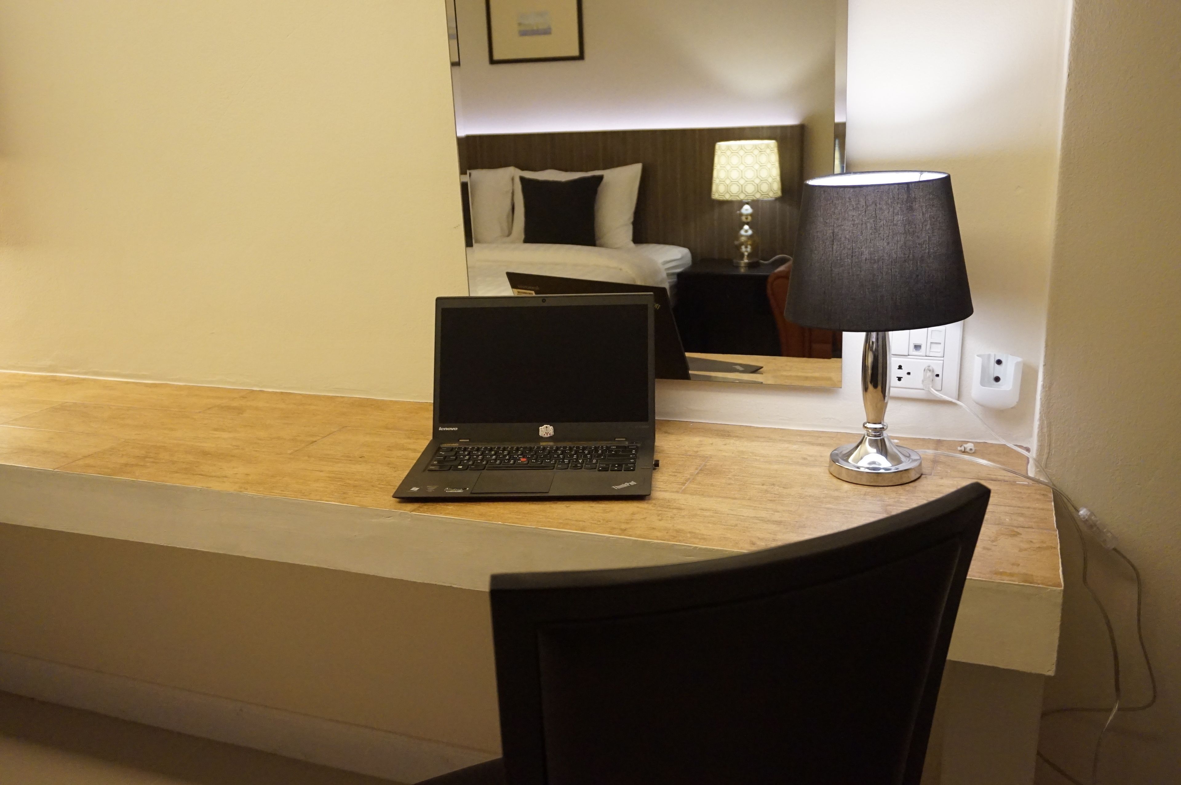 Una habitación de hotel con una laptop sobre un escritorio, una lámpara, una cama y una mesita de noche.