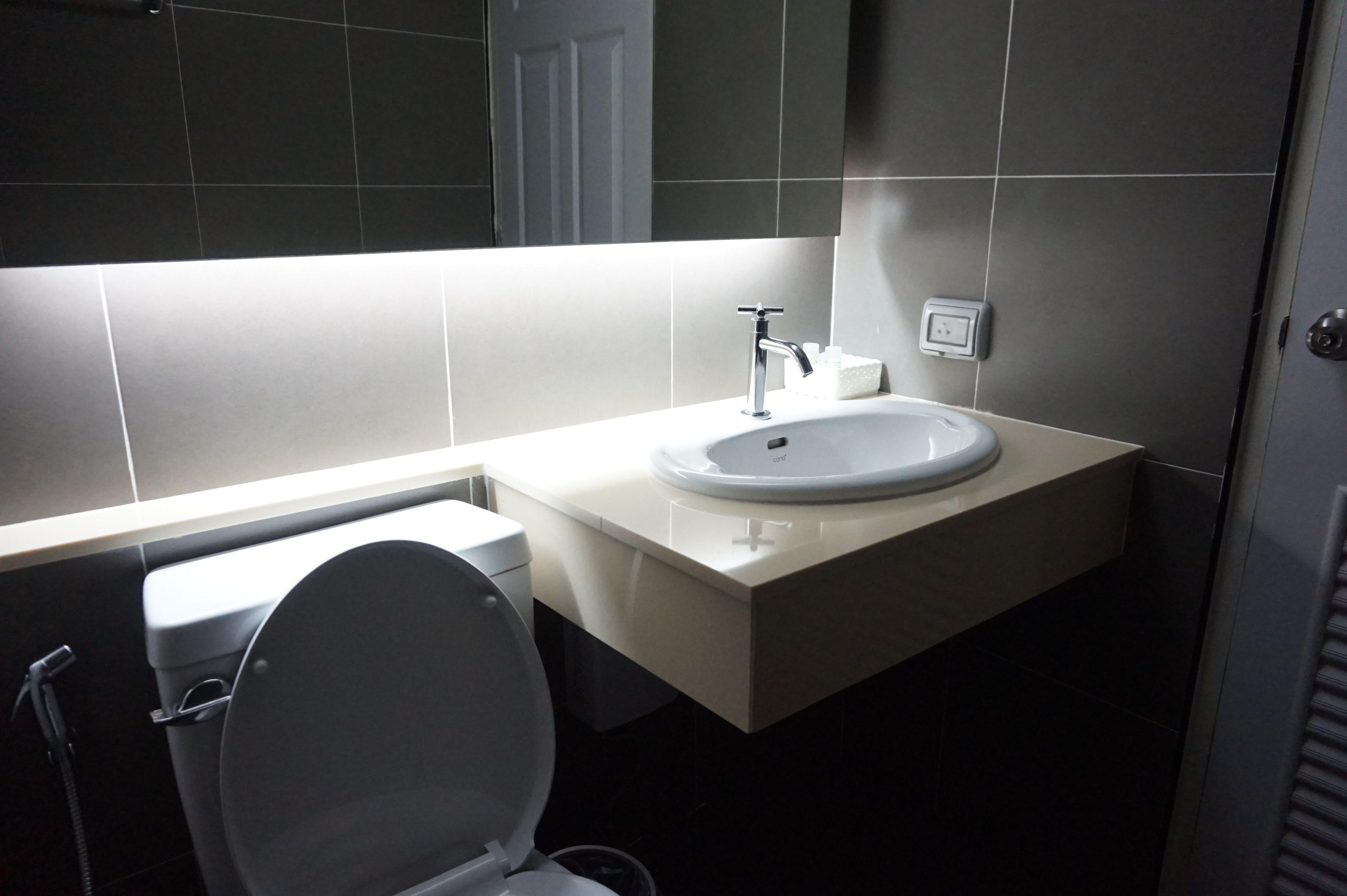 A modern bathroom with a white toilet, a sink with a chrome faucet, and a mirror above the sink.