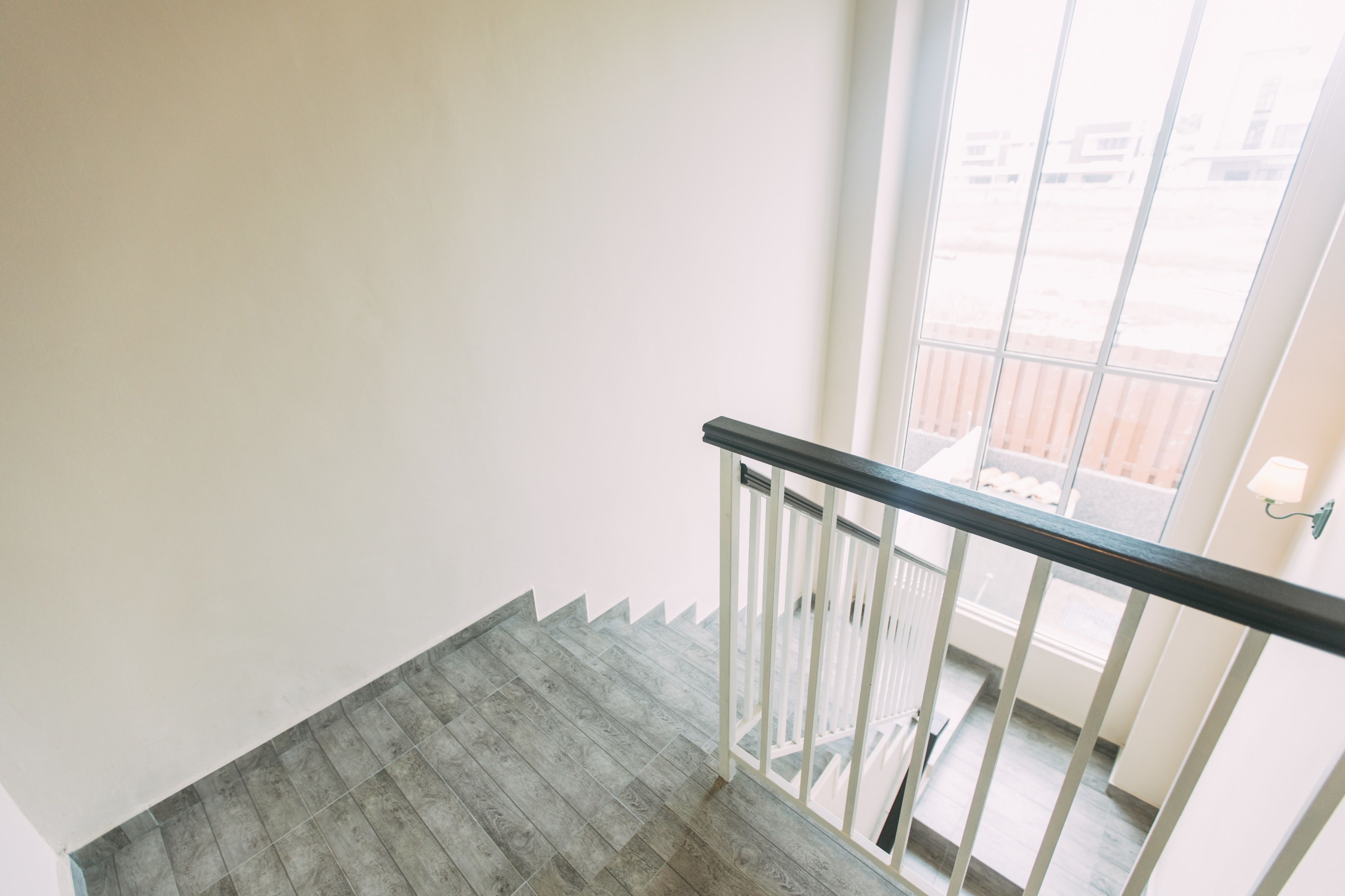 A staircase with a wooden floor and white walls, leading to an outdoor area with a railing and a view of buildings.