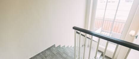 A staircase with a wooden floor and white walls, leading to an outdoor area with a railing and a view of buildings.