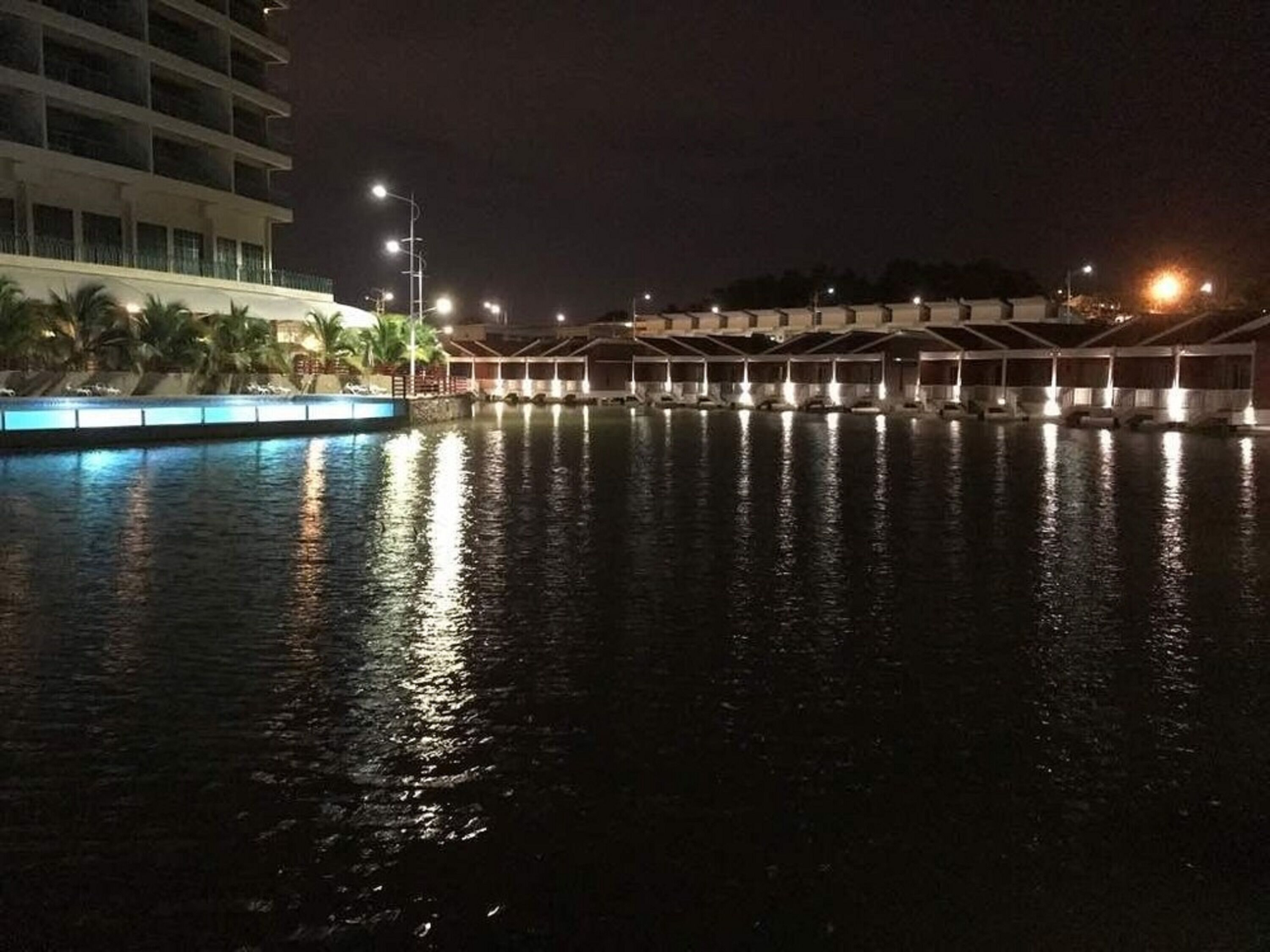 A nighttime view of a hotel with a pool, reflecting the lights and buildings.
