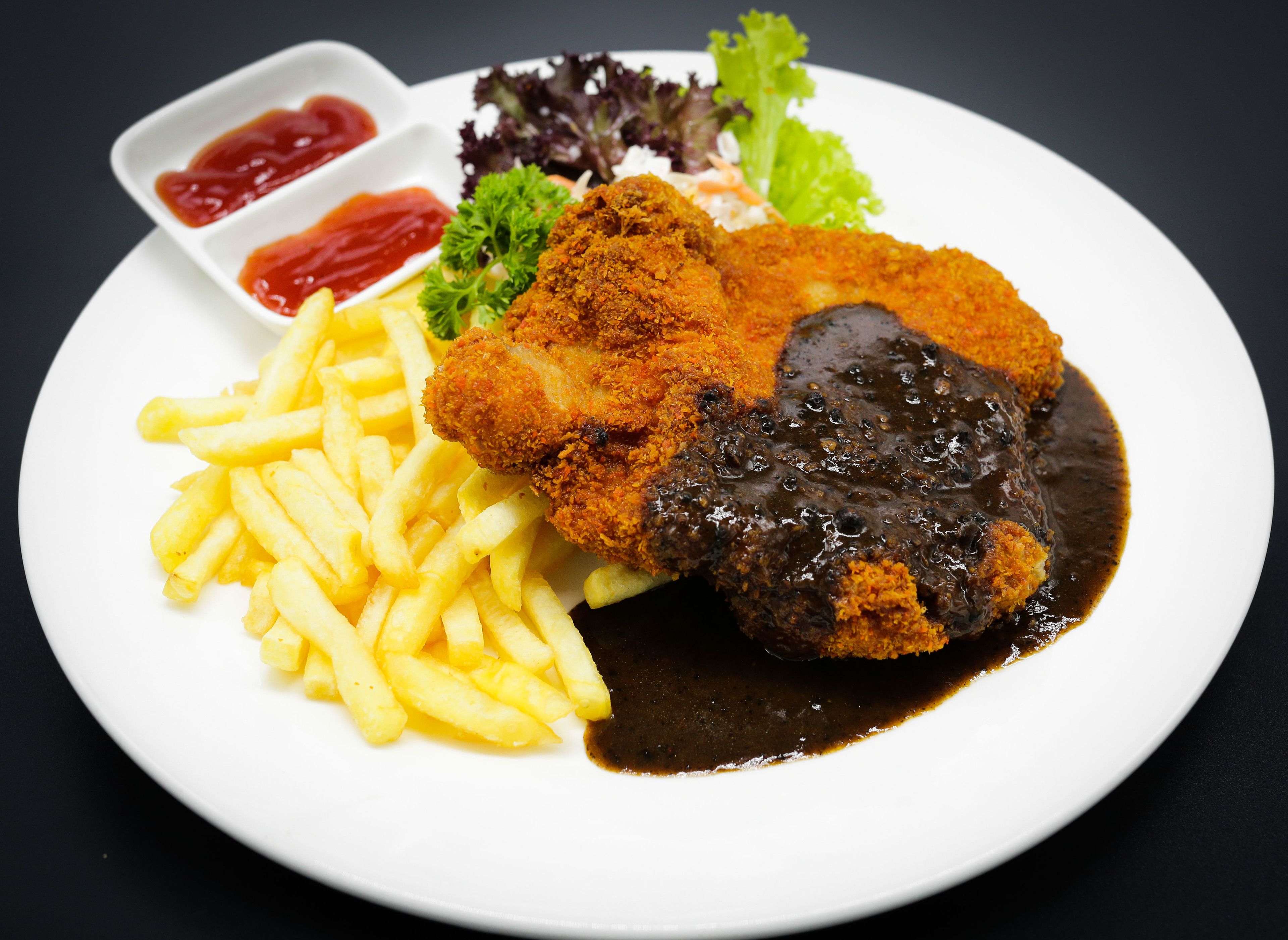 A plate with a breaded and fried cutlet, French fries, and a dark sauce.