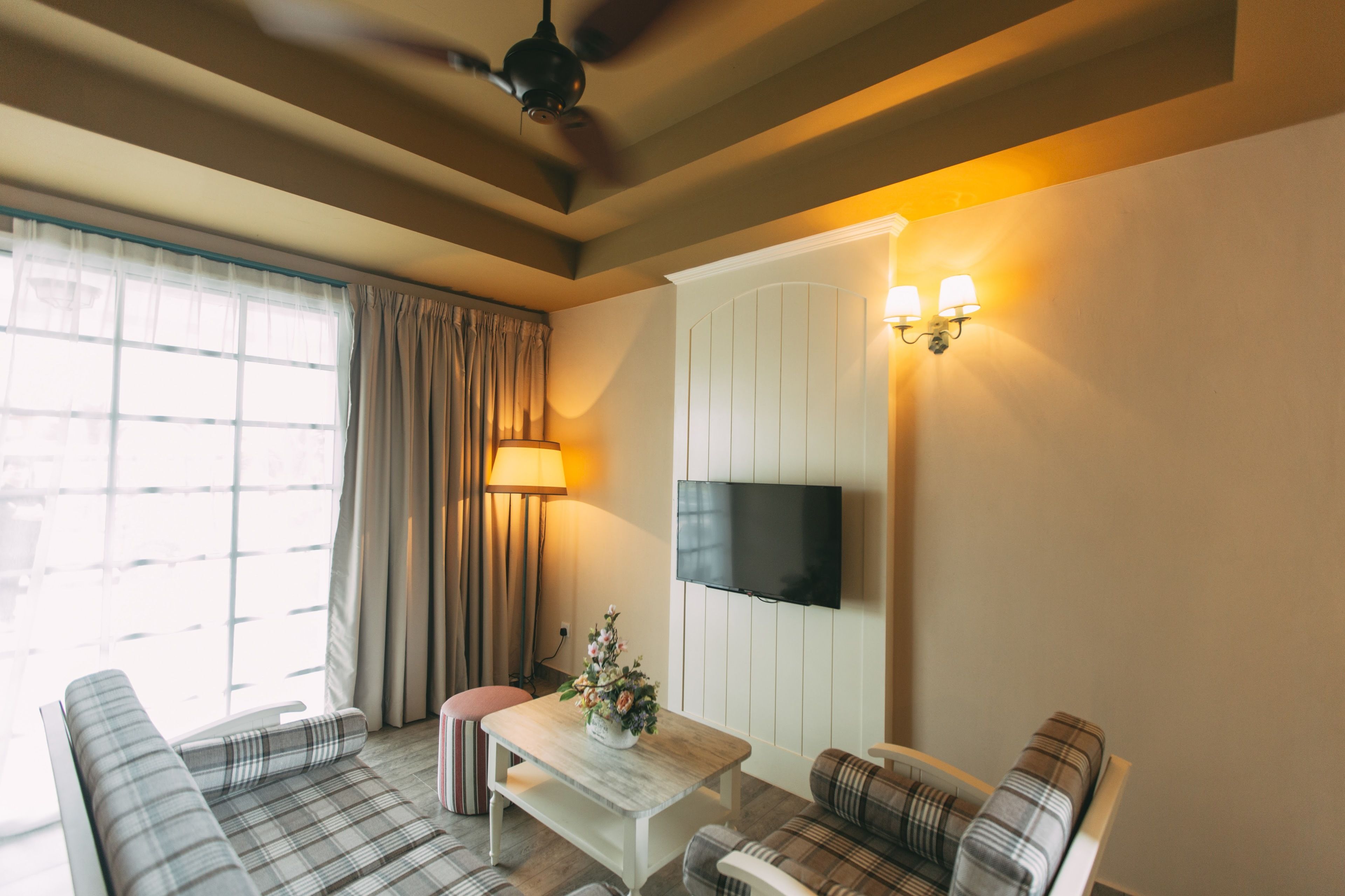 A living room with a sofa, a coffee table, a TV mounted on the wall, and a ceiling fan.