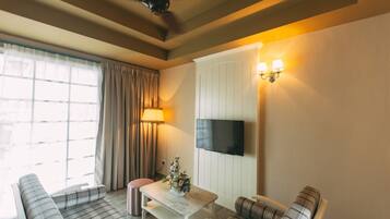 A living room with a sofa, a coffee table, a TV mounted on the wall, and a ceiling fan.