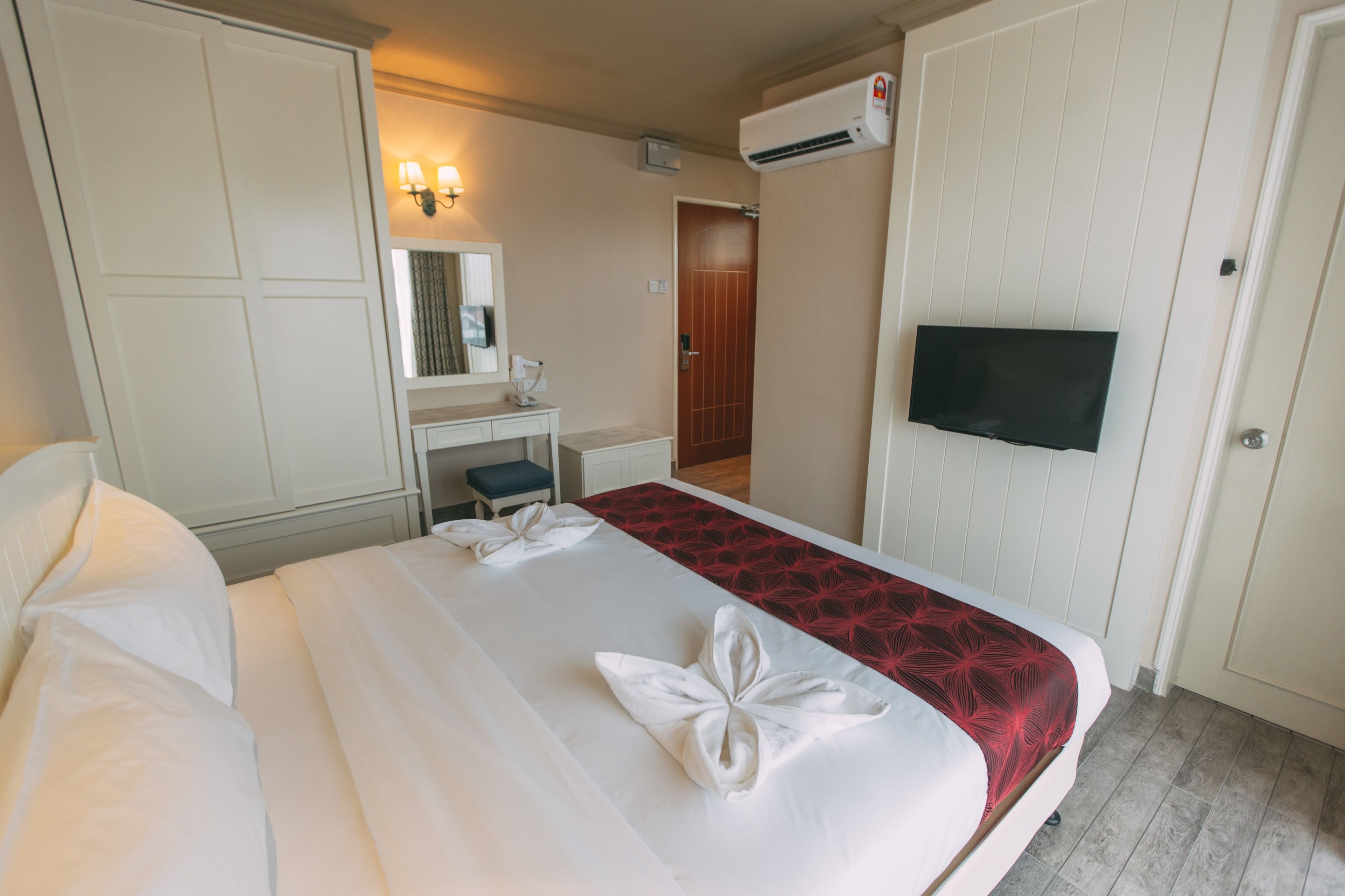 Habitación de hotel con una cama, un escritorio con silla, un espejo, un equipo de aire acondicionado y una televisión.