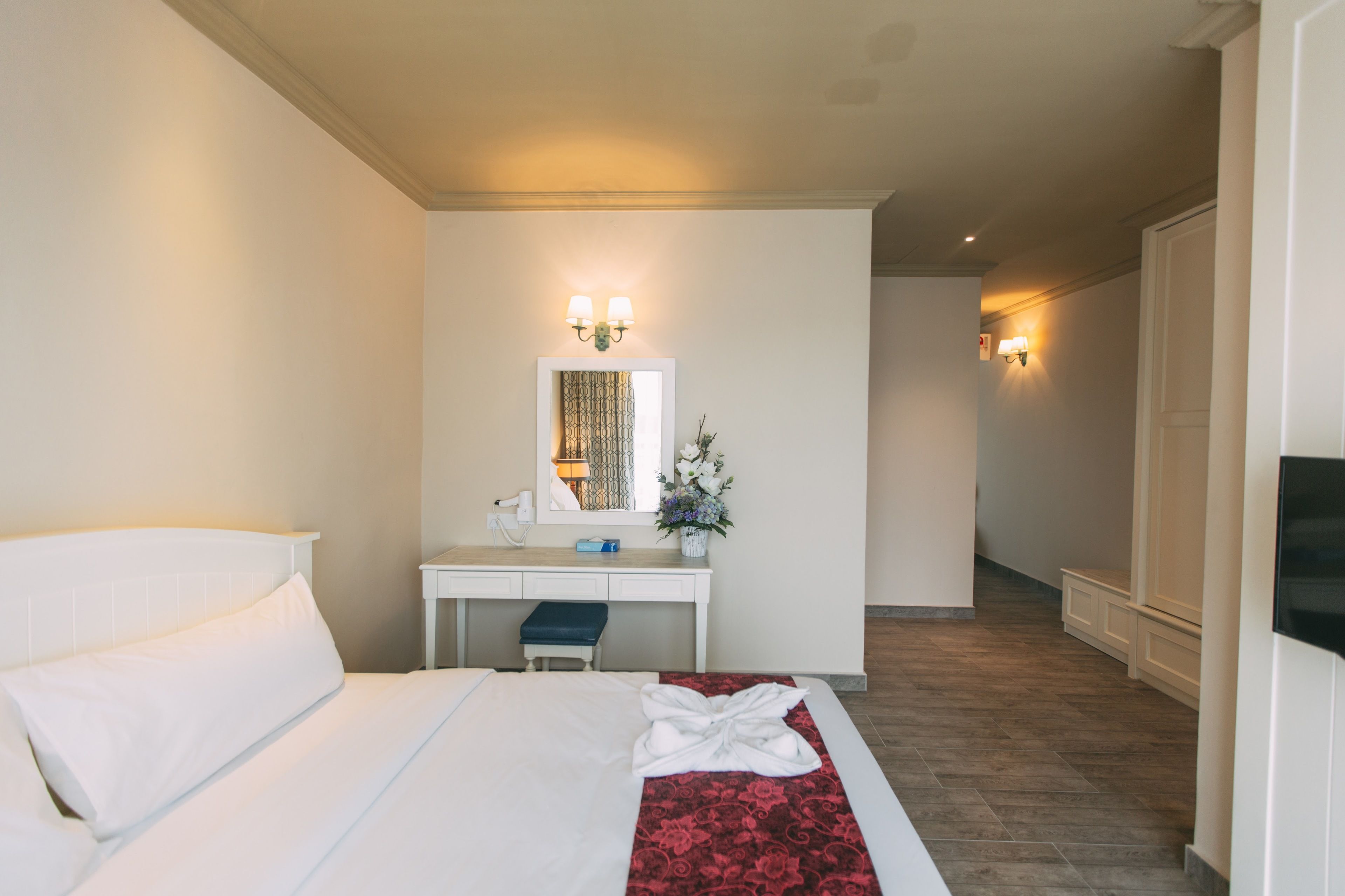 A hotel room with a bed, a desk, a chair, a mirror, and a small table with a vase of flowers.