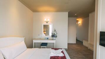 A hotel room with a bed, a desk, a chair, a mirror, and a small table with a vase of flowers.
