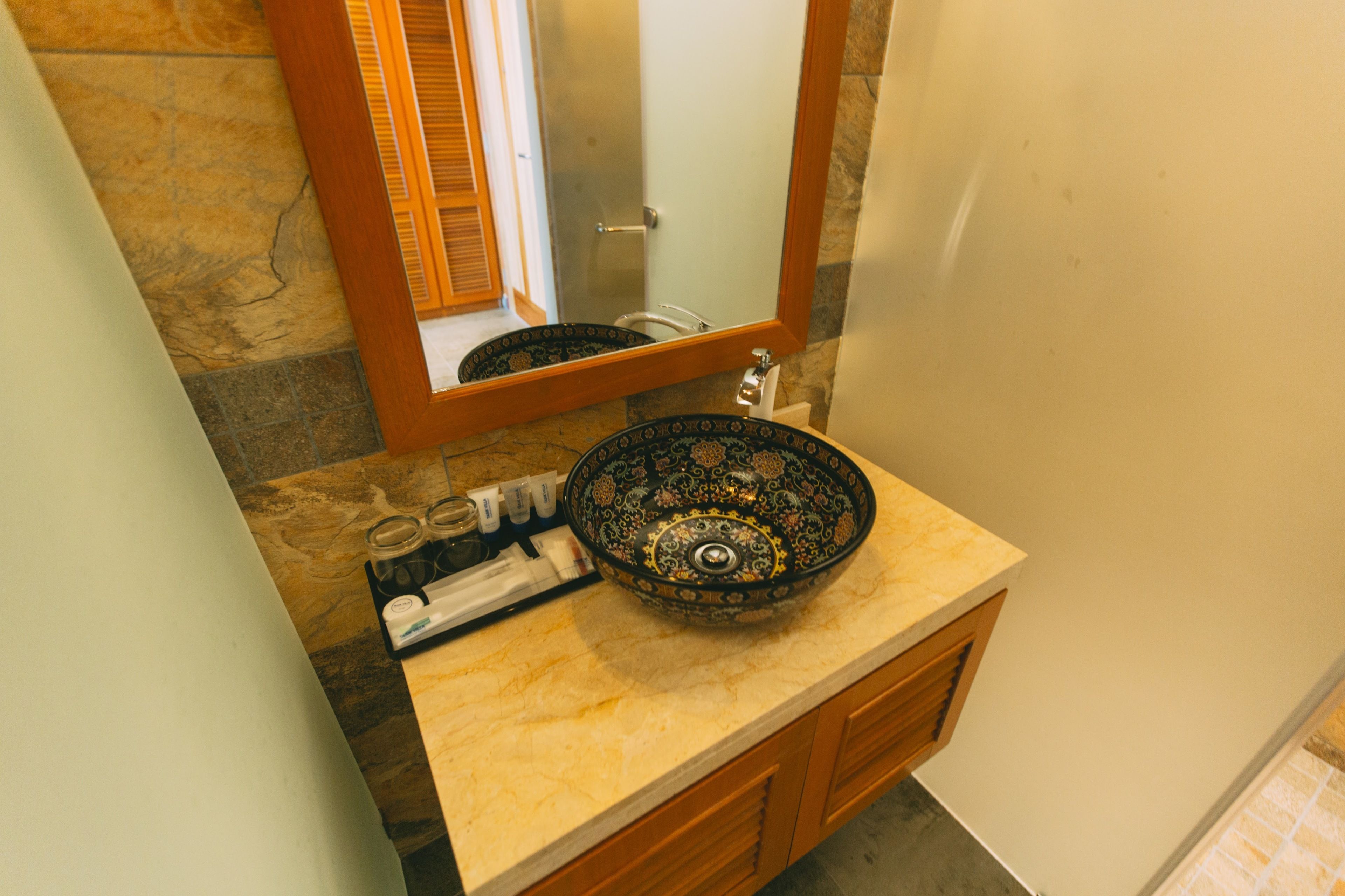 A bathroom with a stone wall, a wooden vanity, a bowl sink, and a mirror.