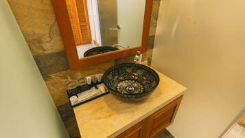 A bathroom with a stone wall, a wooden vanity, a bowl sink, and a mirror.