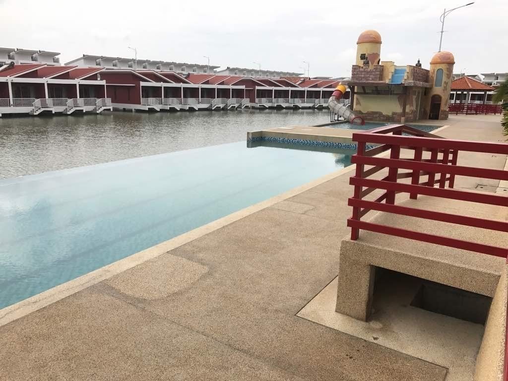 Una piscina con barandilla roja, un tobogán acuático y una fila de edificios con techos rojos al fondo.