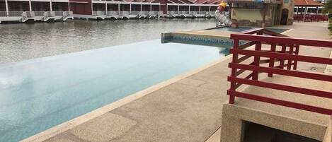 Una piscina con barandilla roja, un tobogán acuático y una fila de edificios con techos rojos al fondo.