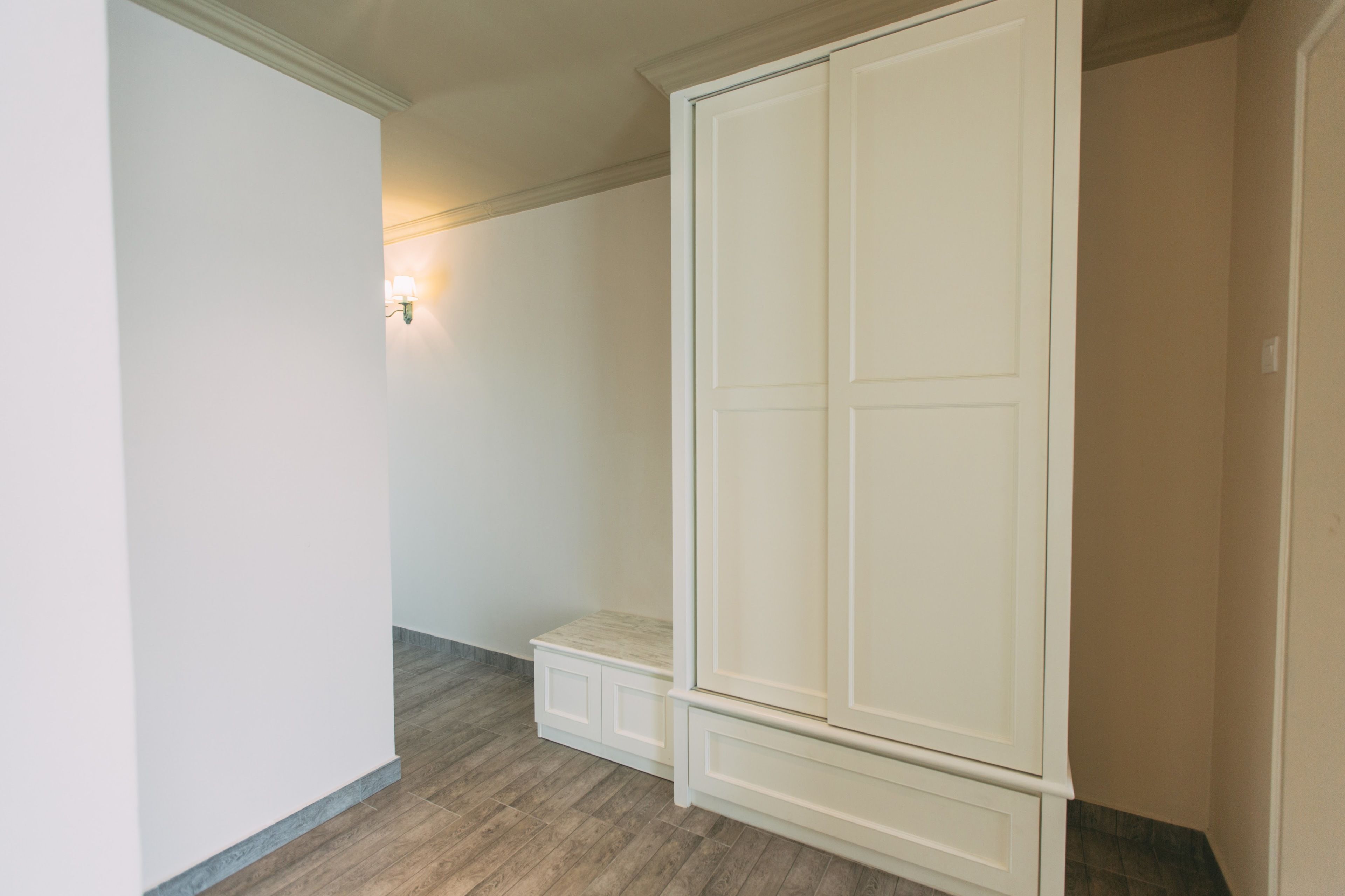 Una habitación con un armario blanco grande, un banco y una lámpara fijada a la pared.