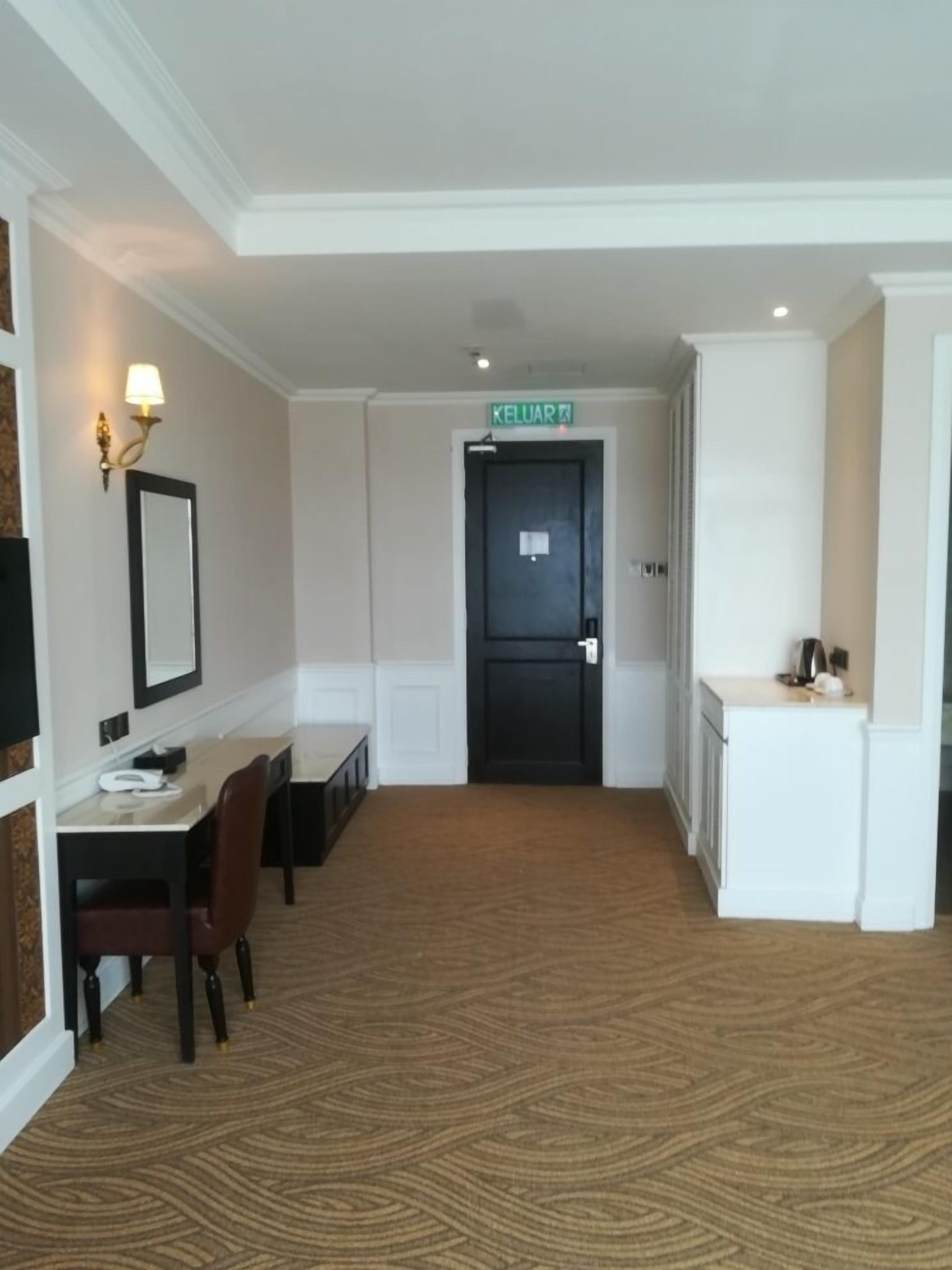 A hotel room with a desk, chair, and a kitchenette area.