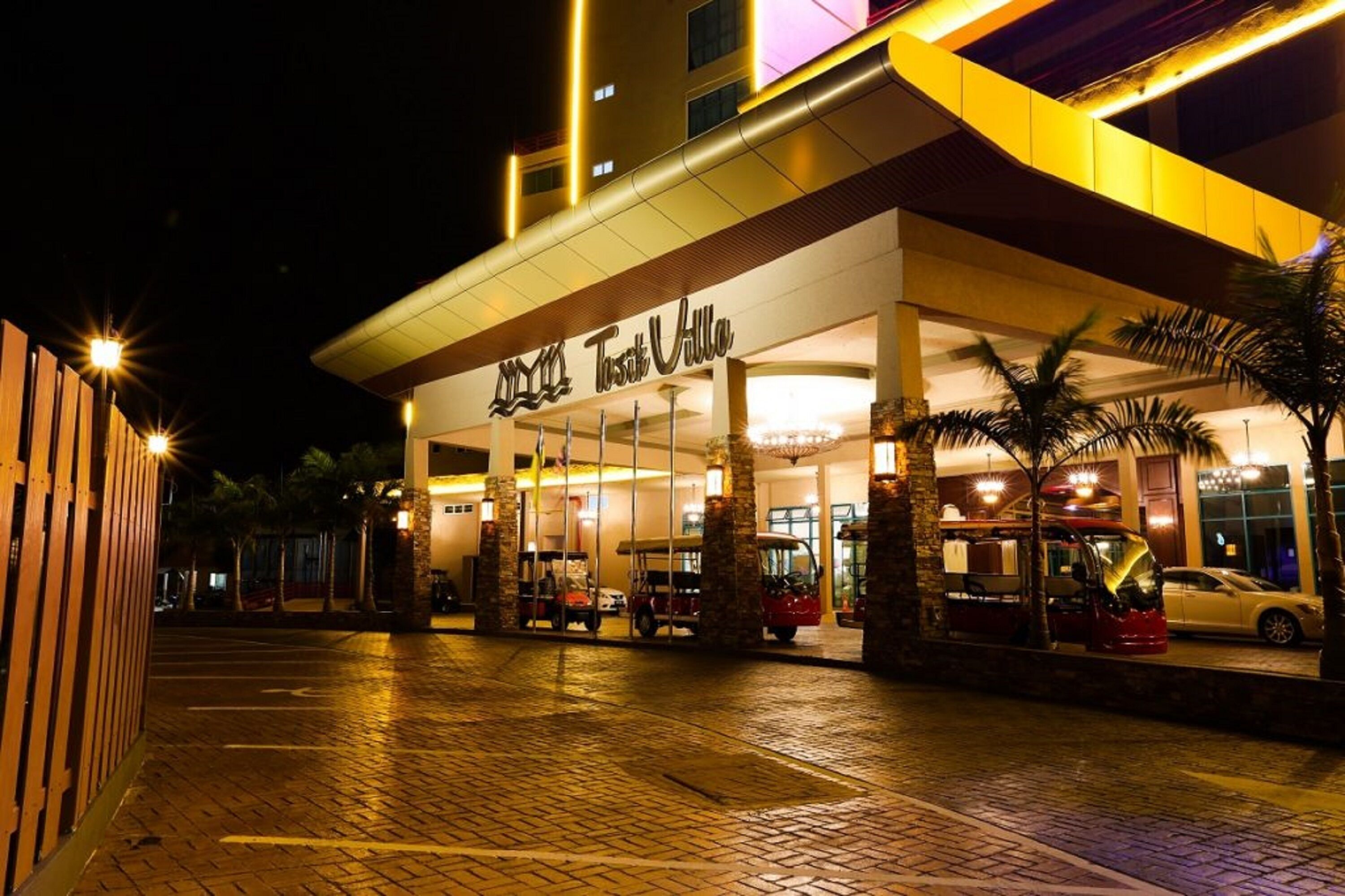 A hotel entrance with a covered walkway, palm trees, and parked vehicles.