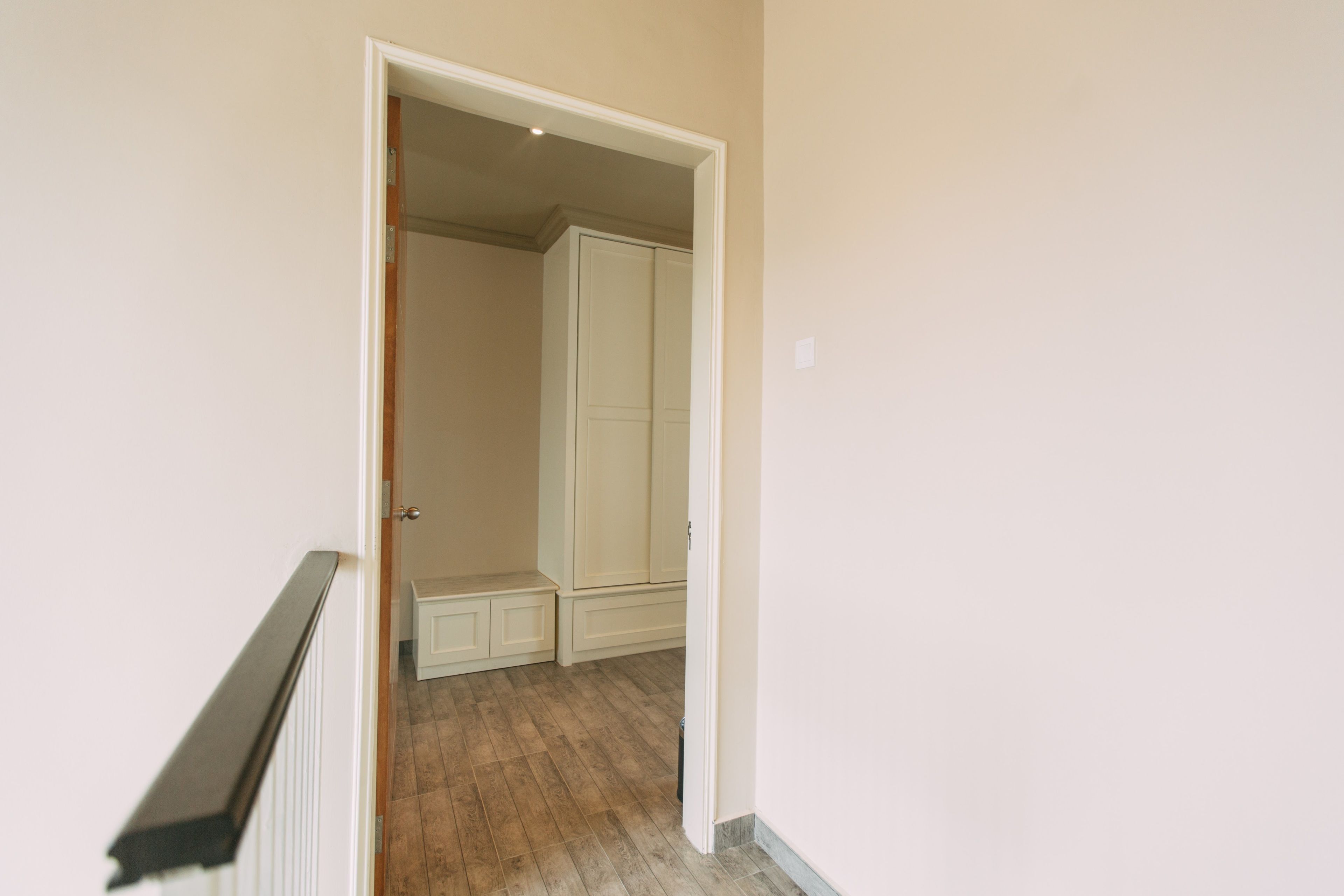 A hallway with a wooden floor, a white door, and a white wardrobe.