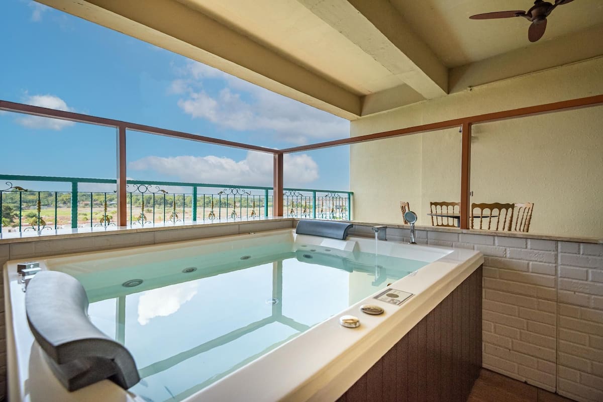 A spa area with a large bathtub, a ceiling fan, and a view of the outdoors.