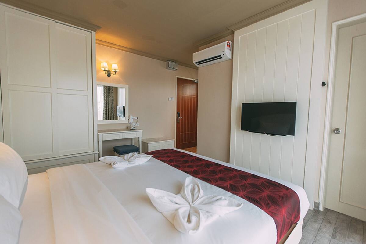 A hotel room with a bed, a desk, a mirror, an air conditioning unit, and a television.
