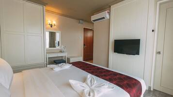 A hotel room with a bed, a desk, a mirror, an air conditioning unit, and a television.