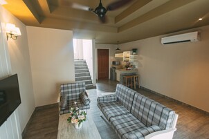 Una sala de estar con un sofá, una mesa de centro con flores, un televisor y una escalera que lleva a una cocina.