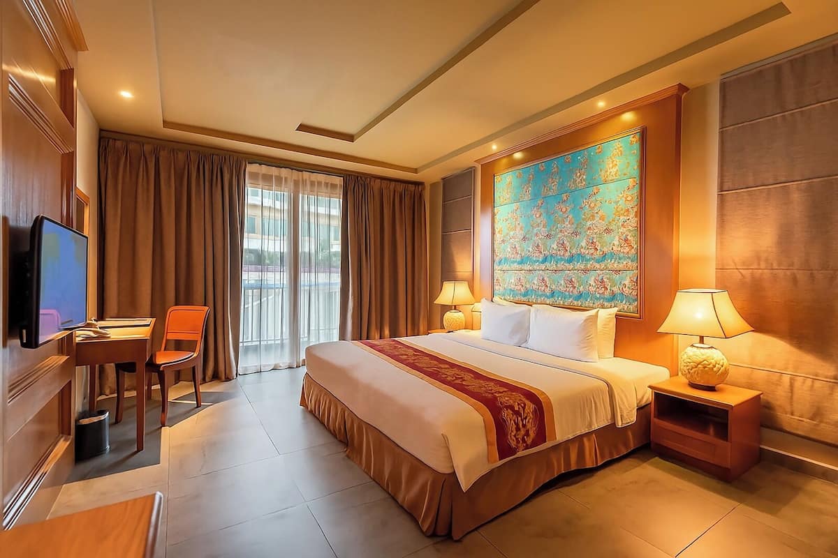 A hotel room with a large bed, a desk with a chair, a television, and a window with curtains.