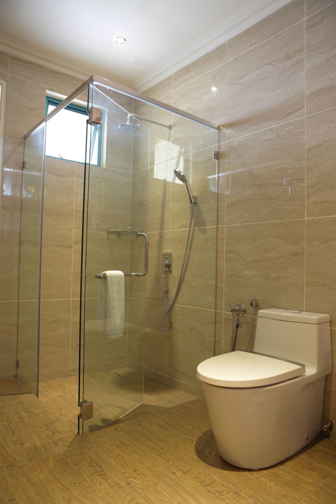 A modern bathroom with a glass-enclosed shower, a toilet, and a wooden floor.