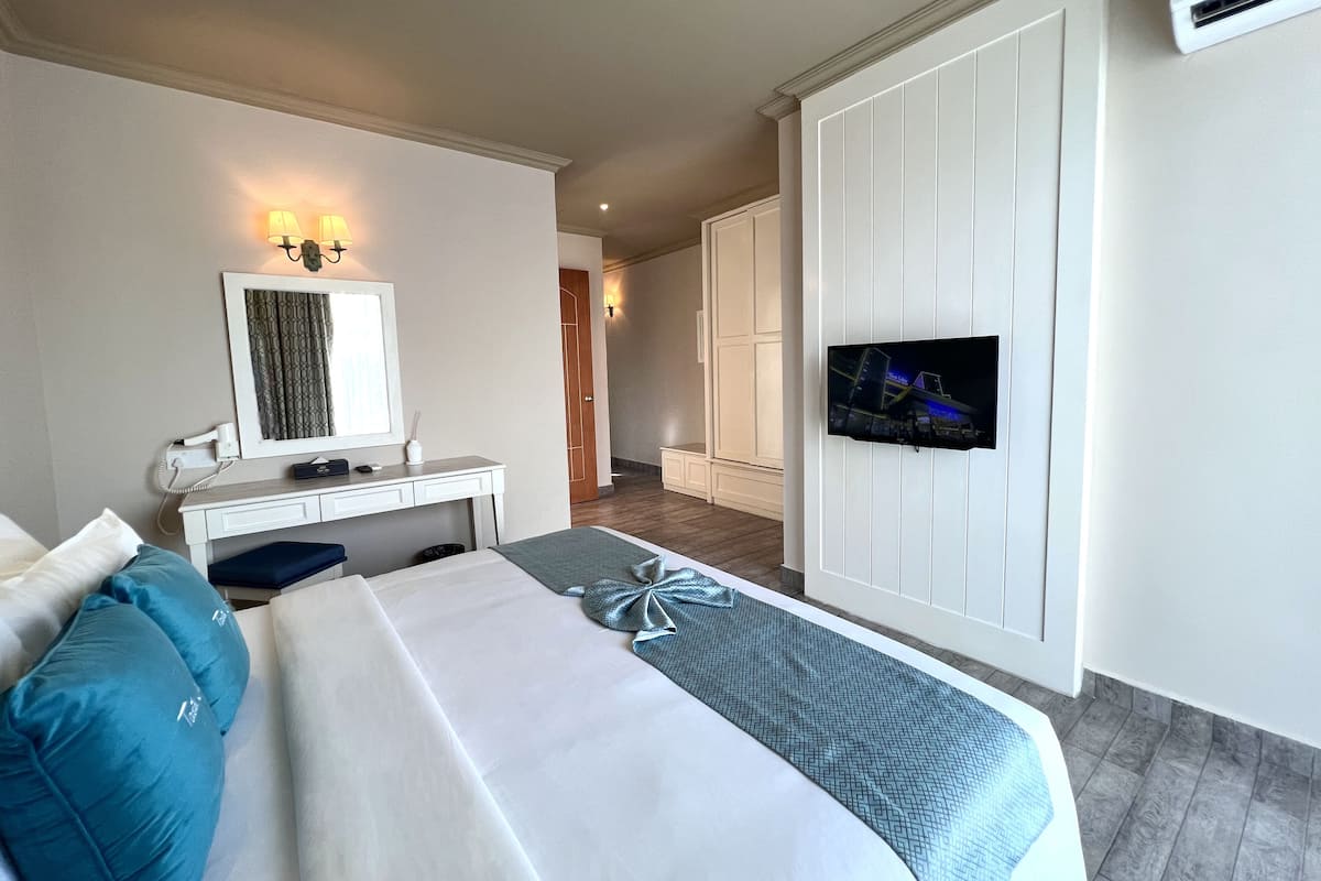 A hotel room with a bed, a desk, a TV mounted on the wall, and a wardrobe.