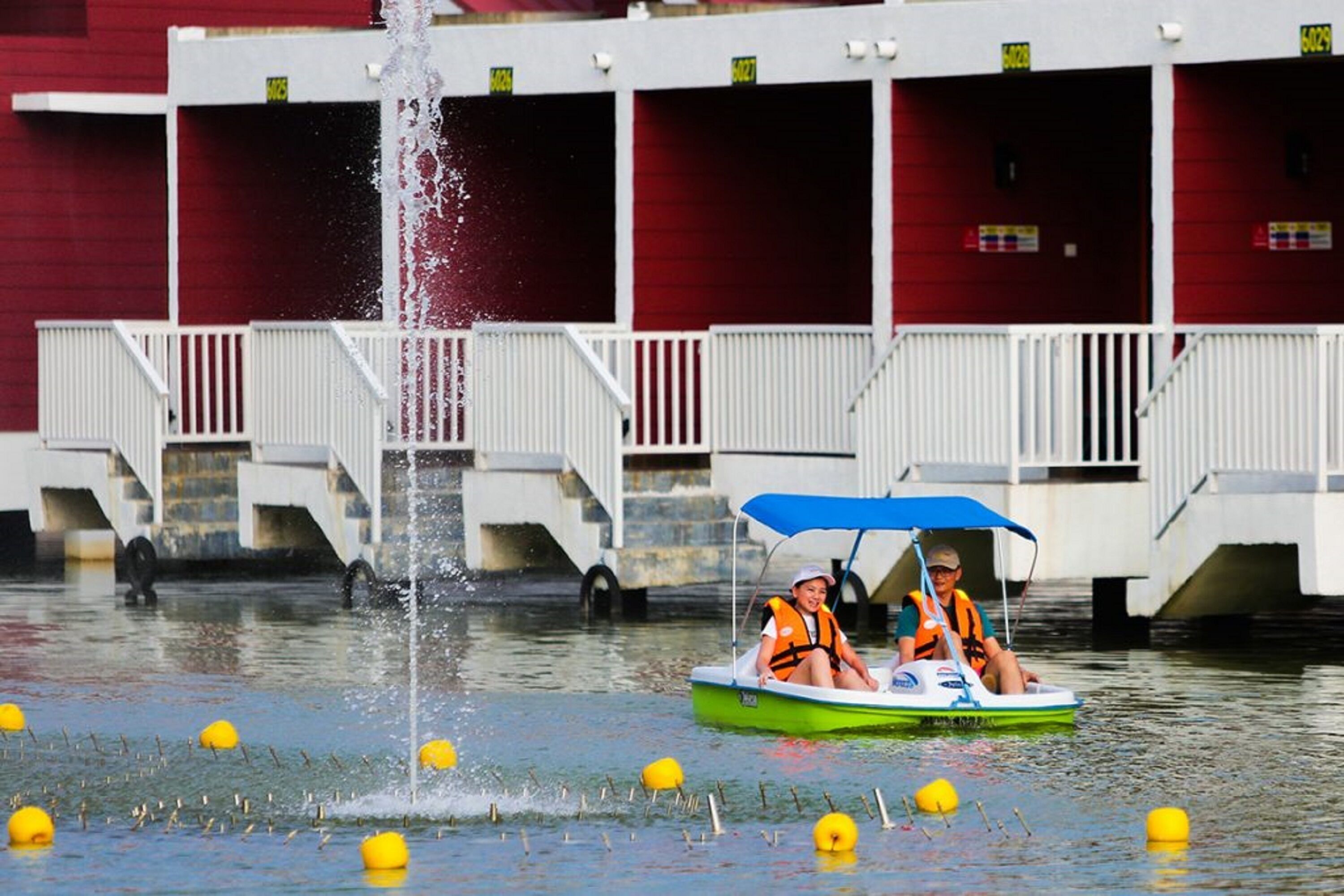 A boat ride with a fountain in the background and a building with balconies.