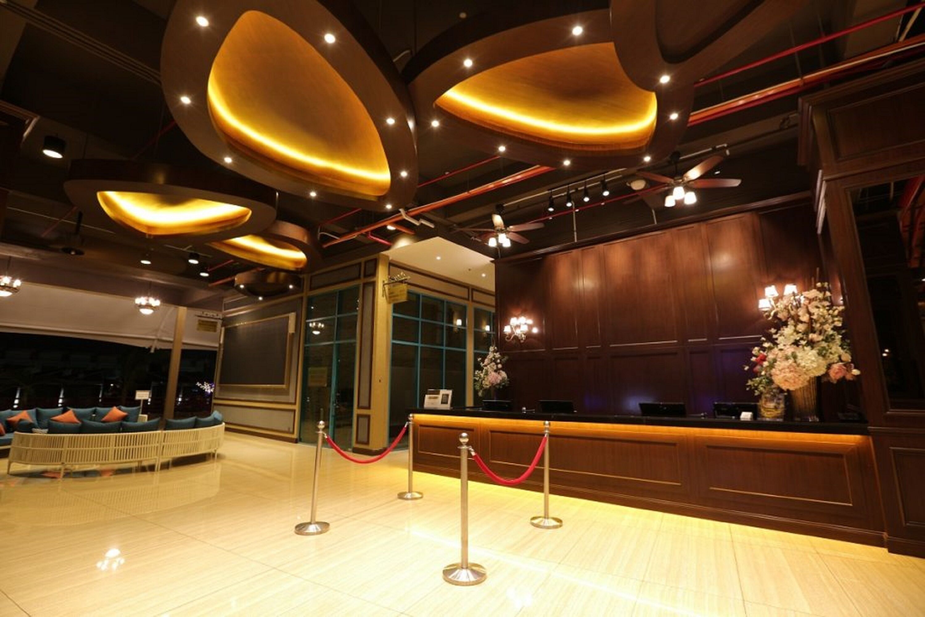 Un vestíbulo de hotel con una recepción, un área de estar con sillones acolchados y un arreglo floral decorativo.
