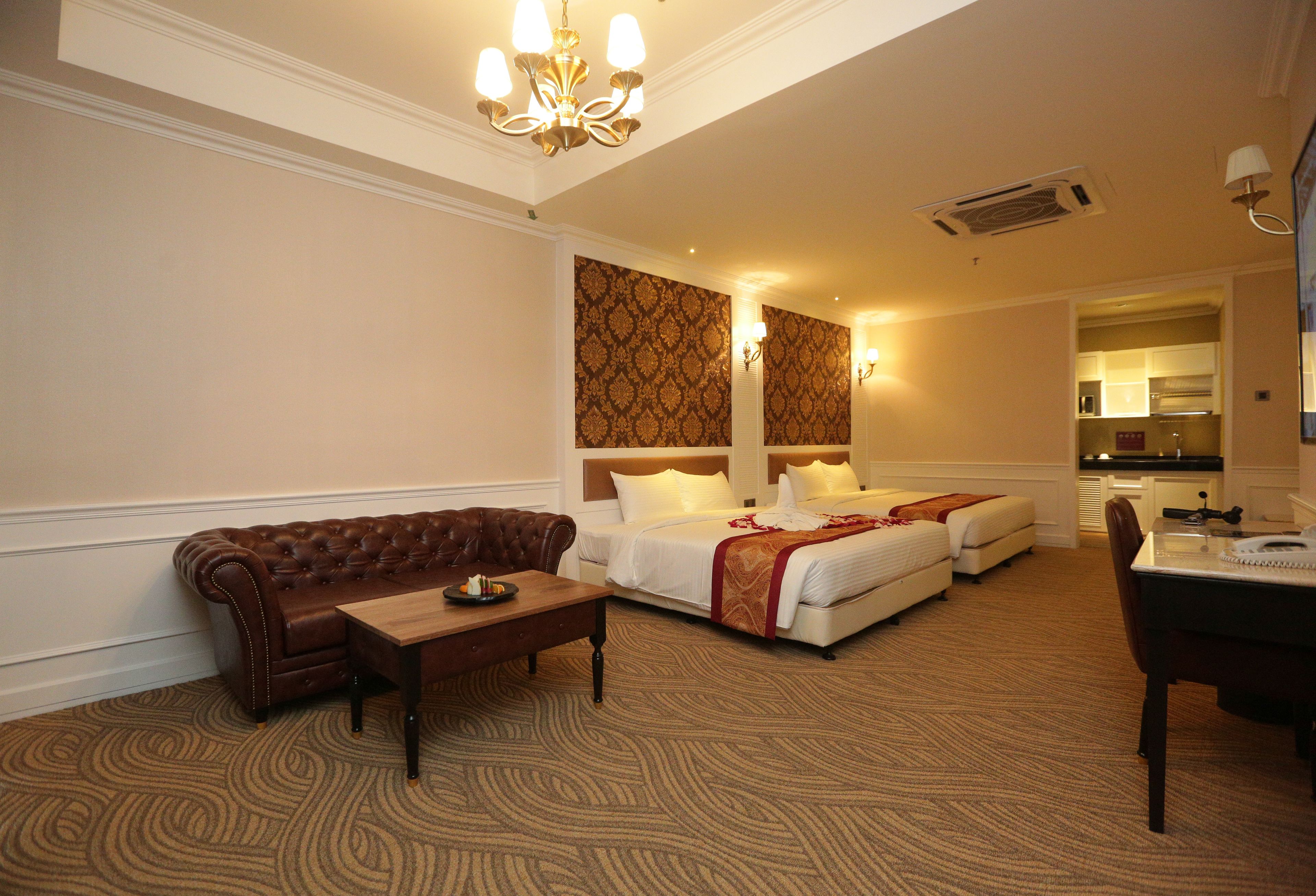 Ein Hotelzimmer mit braunem Ledersofa, einem Holztisch, einem Doppelbett mit rotem und weißem Überwurf, einem weißen Kopfteil und einem kleinen Schreibtisch mit Stuhl.