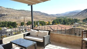 A balcony with wicker furniture, a glass table, and a view of a mountainous landscape. - Monte Cappa Cave House (Ürgüp)