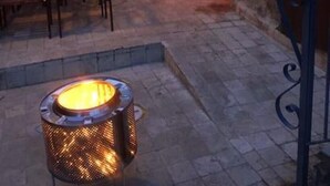 En utomhusplats med en uteplats, murar av sten, trädgårdsmöbler och en centralt placerad eldstad.