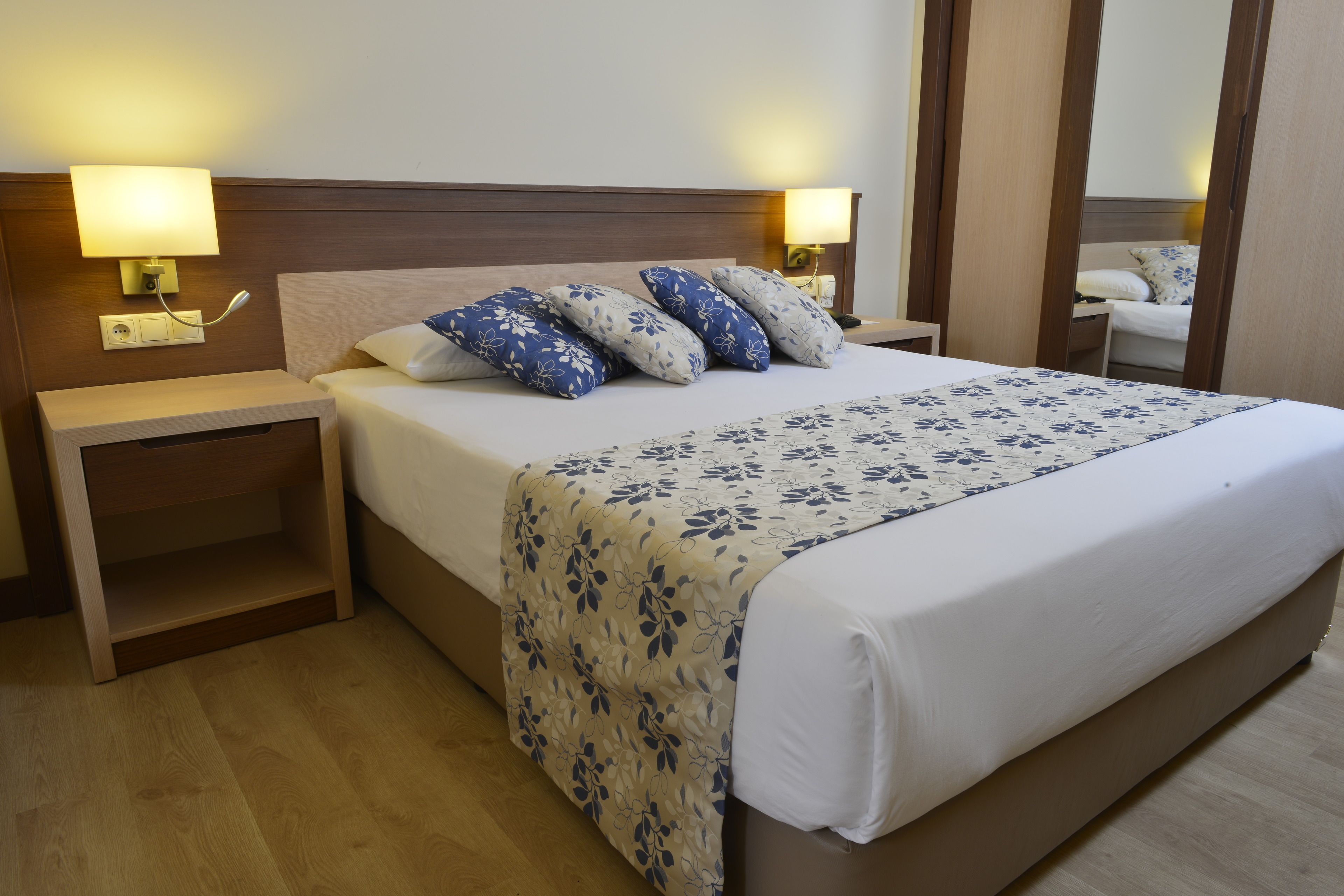 A hotel room with a bed, nightstands, lamps, and a mirror.