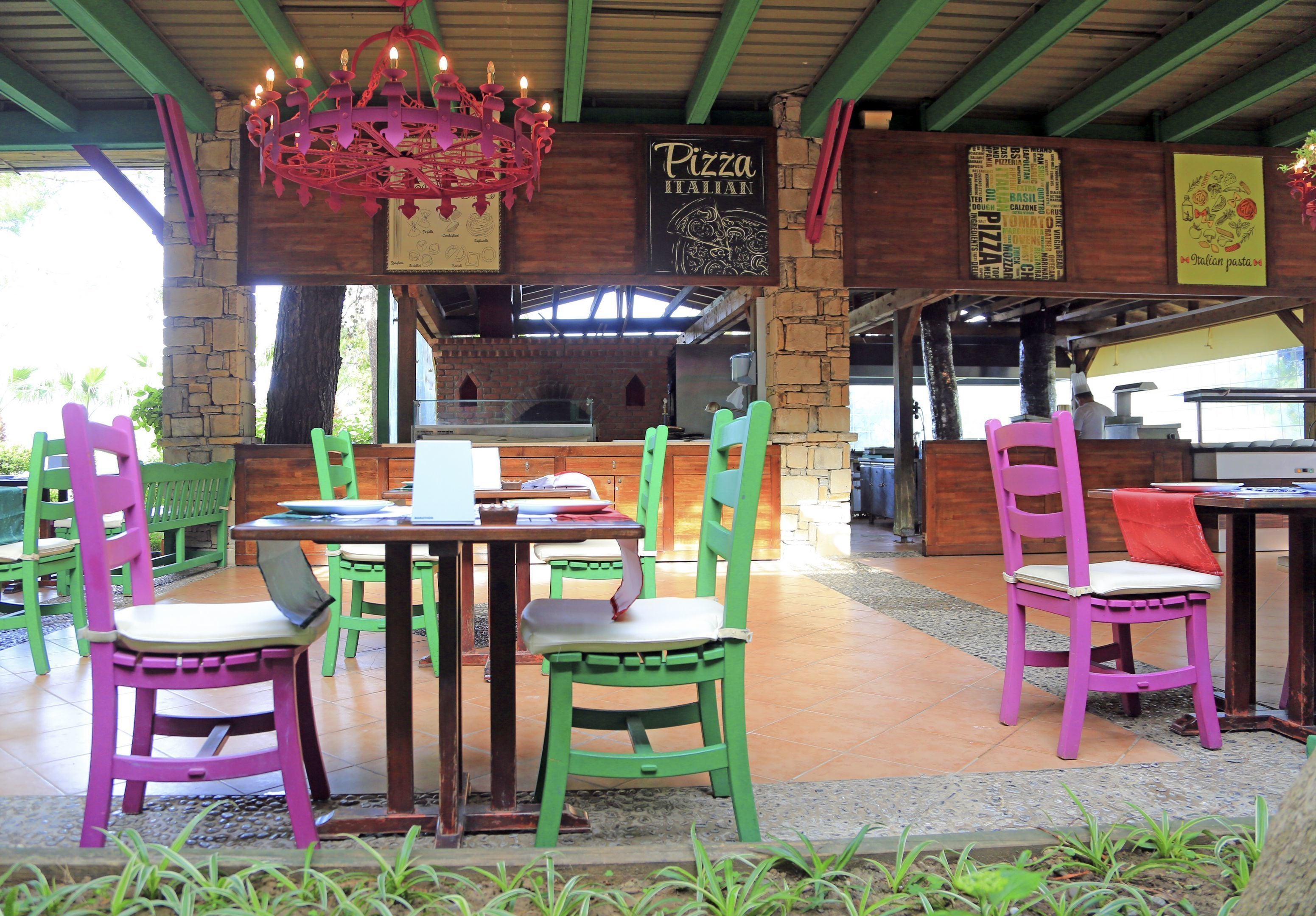 Un espacio exterior para comer con mesas y sillas de madera, un letrero de pizza y una pared de ladrillo.