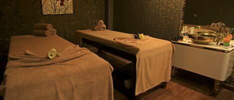 A spa room with two massage tables, towels, a sink, and a mirror.