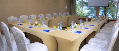 A conference room with a long table, chairs, water bottles, apples, and a projector screen.