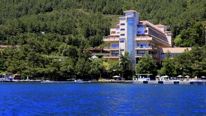 Un hôtel à plusieurs étages, doté de balcons, situé près d’une étendue d’eau où l’on peut trouver des bateaux et un quai.