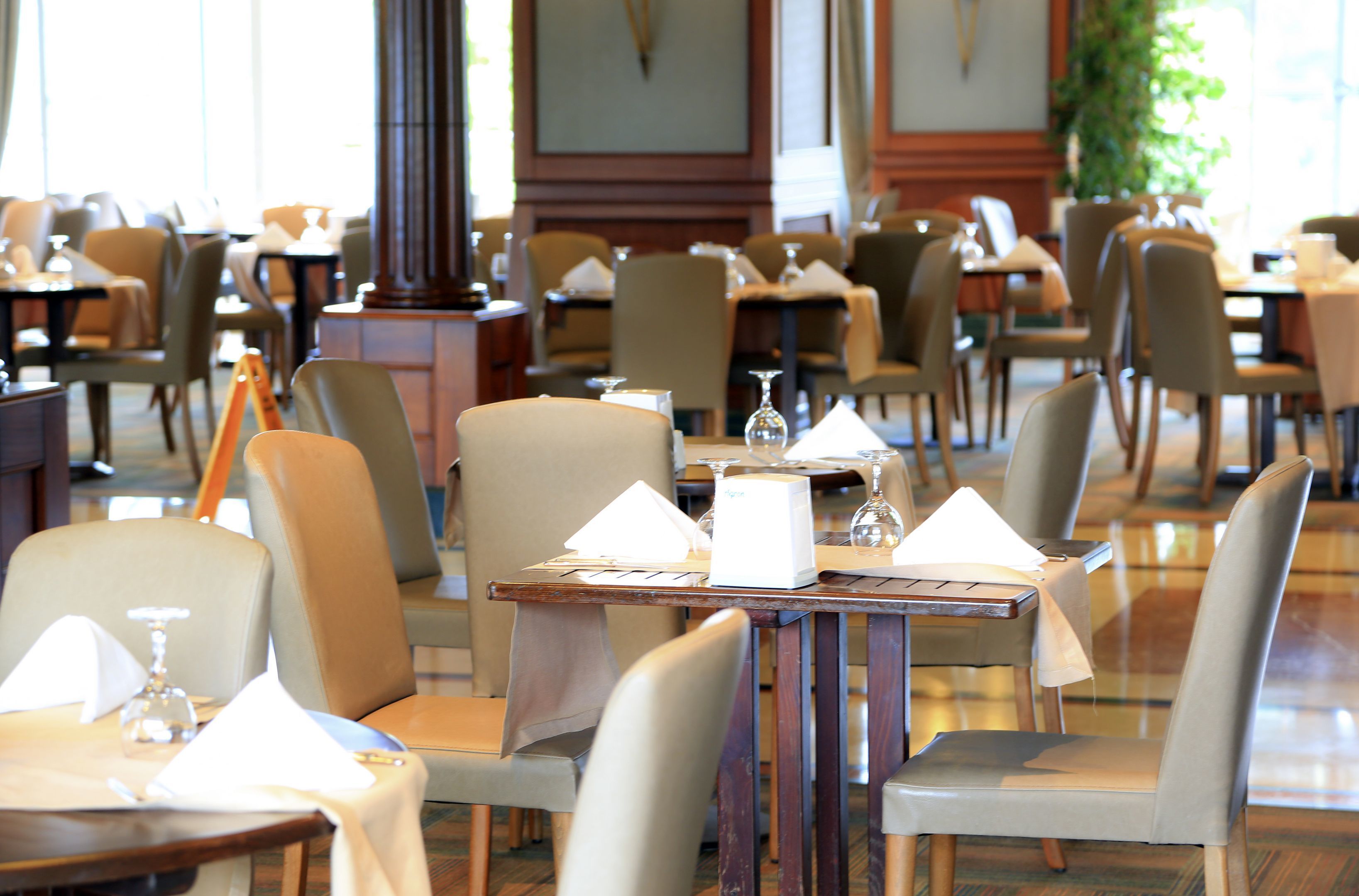 Un restaurante con varias mesas y sillas, cada conjunto con mantel blanco, copas de vino y servilletas.