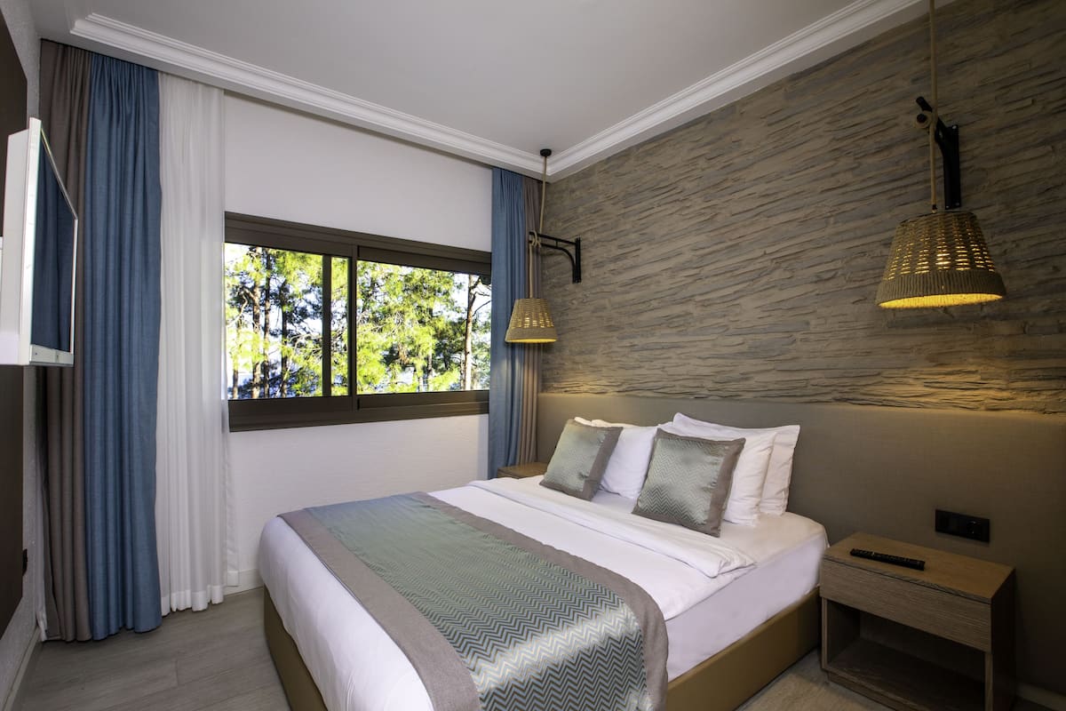 Um quarto moderno com uma cama grande, uma mesinha de cabeceira, uma janela com cortinas e uma parede de pedra.