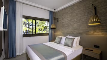 A modern bedroom with a large bed, a nightstand, a window with curtains, and a stone wall.