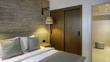 A bedroom with a bed, a wooden headboard, a nightstand, a wall-mounted lamp, and a wooden wardrobe.