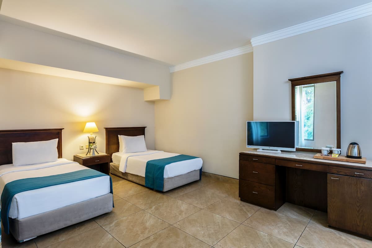 Quarto de hotel com duas camas, uma televisão, uma escrivaninha com cafeteira e um espelho.