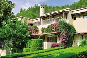A two-story building with a balcony, surrounded by lush greenery and flowering plants.
