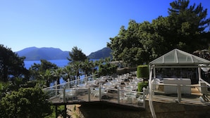 Un espace extérieur aménagé avec des tables et des chaises, offrant une vue sur un plan d’eau et des montagnes.